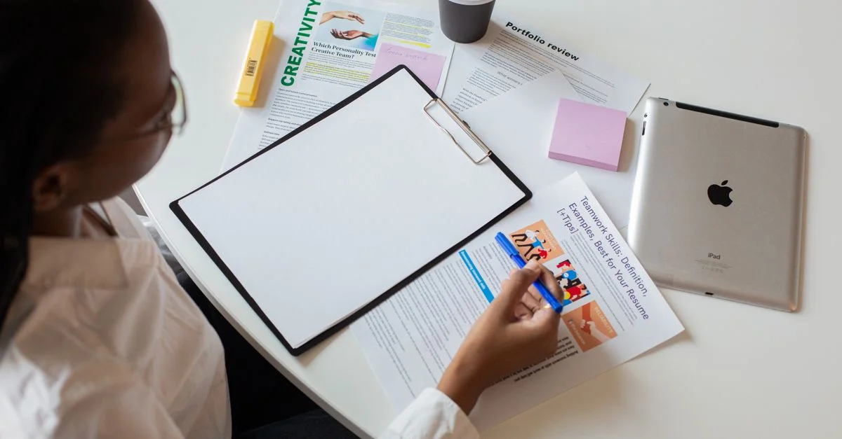 Vue de dessus d'une femme examinant divers documents avec un clipboard sur un bureau.